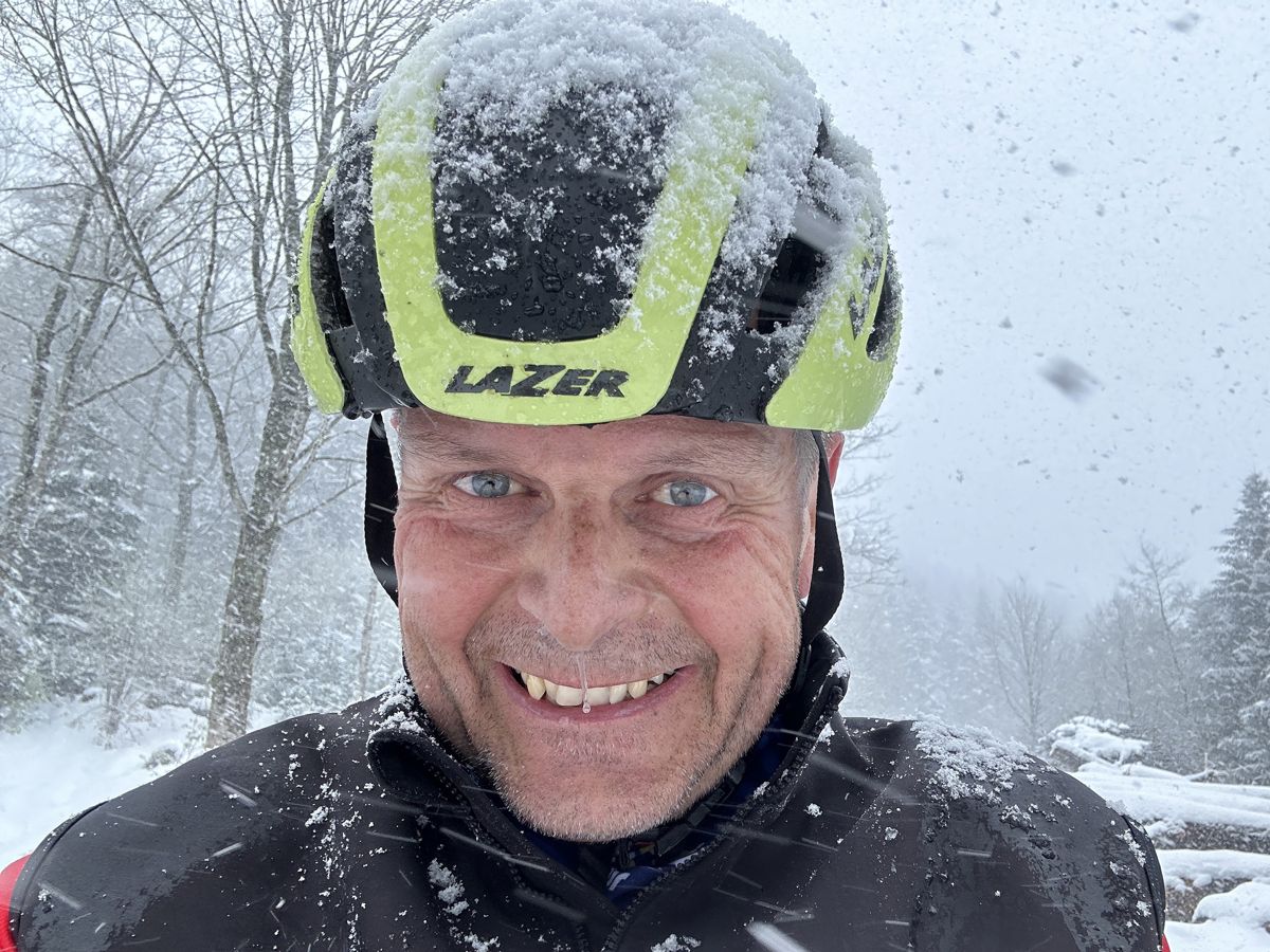 Martin Platter lacht mit verschneitem Velohelm im Schneegestöber