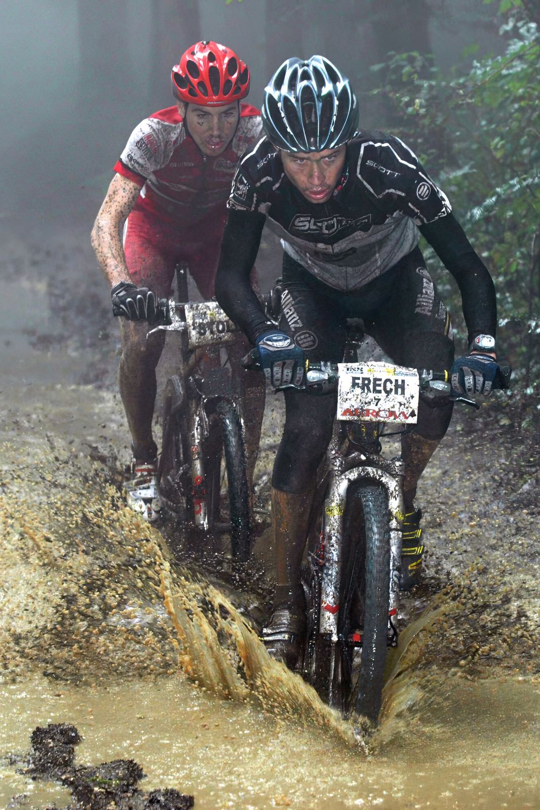 Frédéric Frech vor Thomas Stoll, beide verschlammt, fahren an der iXS-Classic 2005 in Schleitheim durch eine Pfütze im nebligen Wald