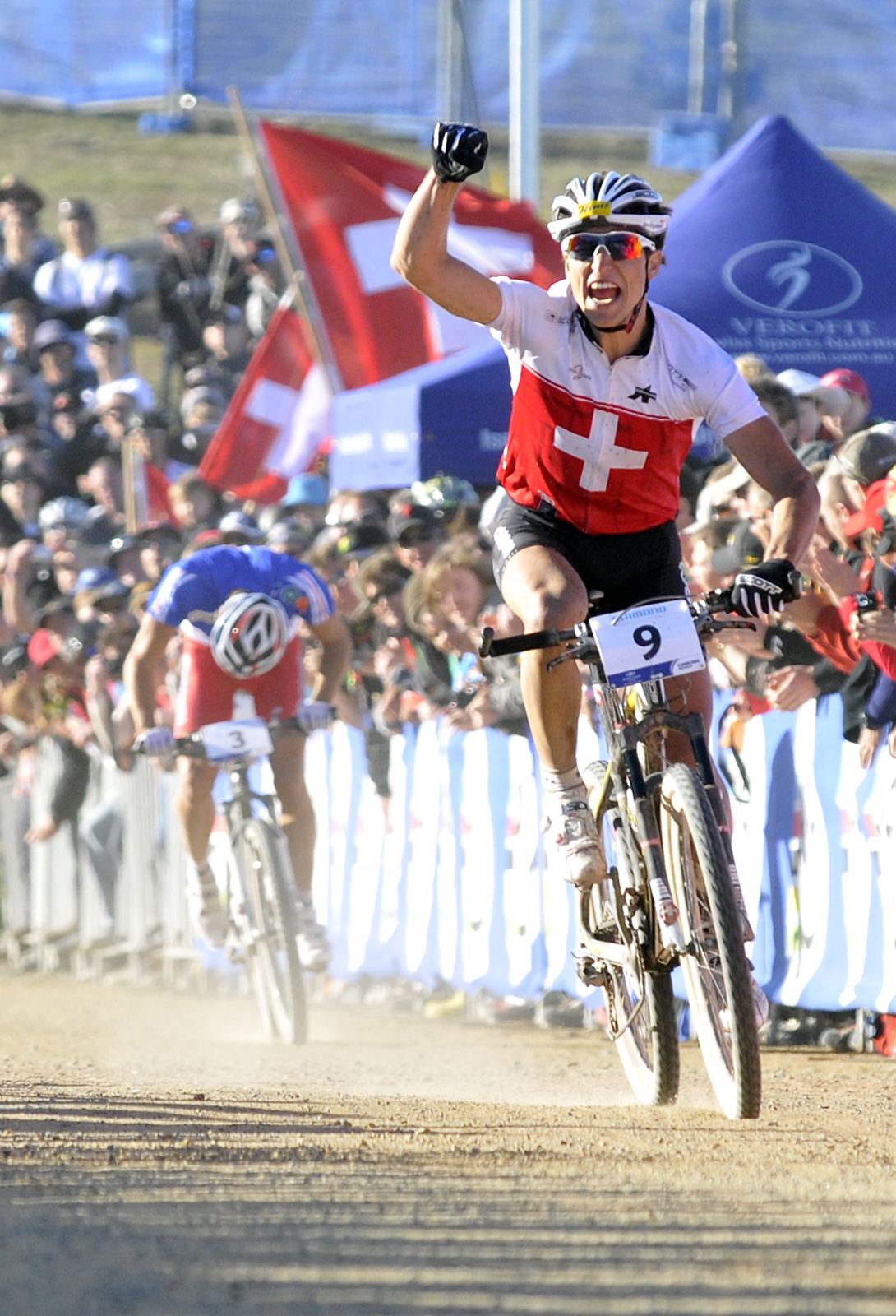 Nino Schurter im Schweizer Trikot jubelt mit geballter Faust im Ziel der WM 2009 in Canberra, dahinter Julien Absalon mit Nummer 3